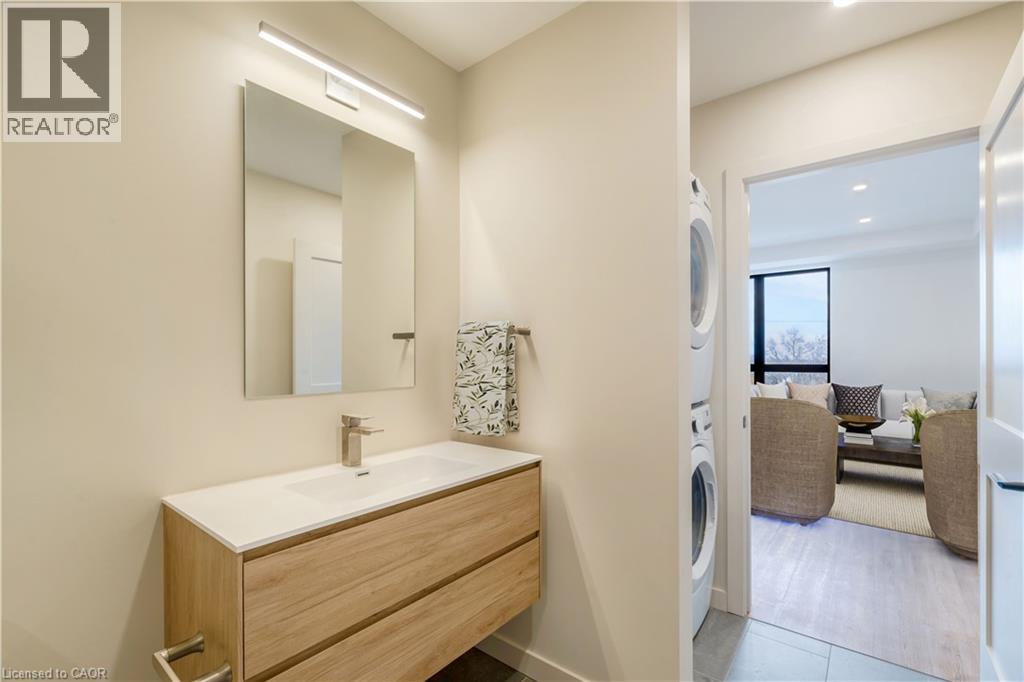 A bathroom with a sink and mirror on the left and a living room with a couch and a window on the right.