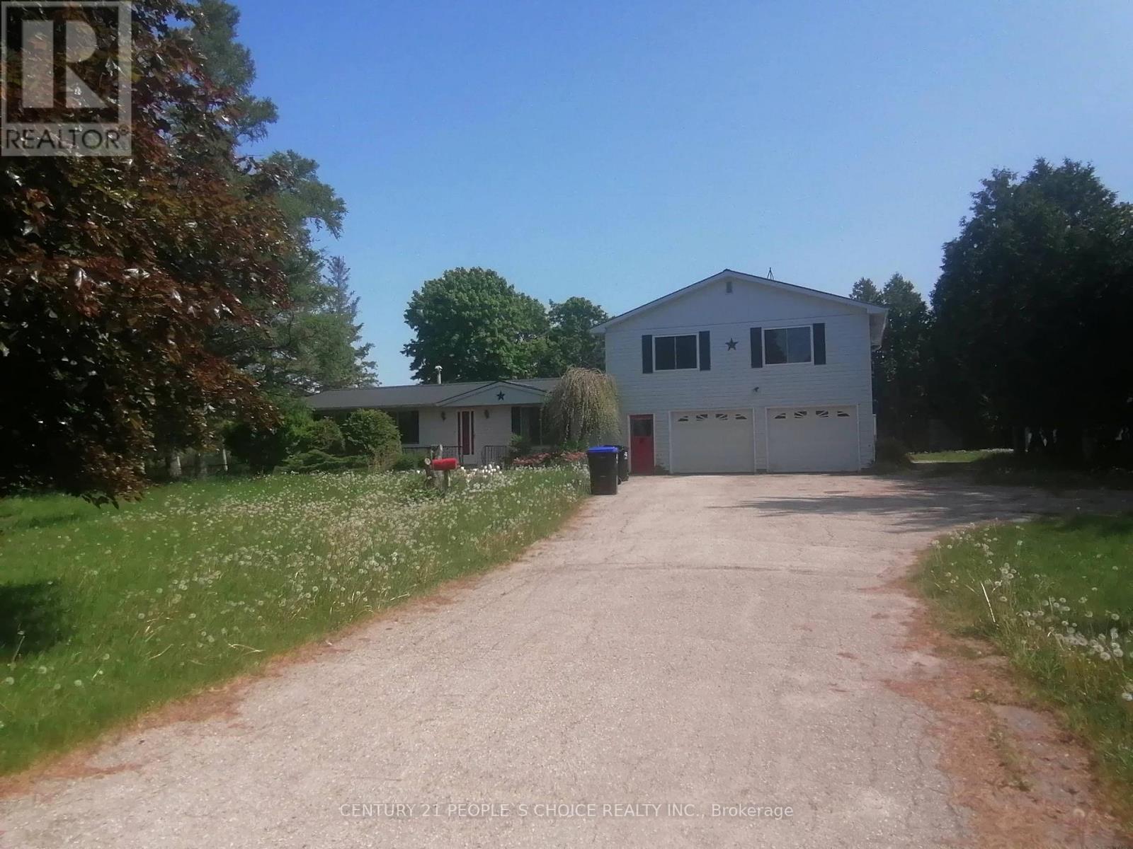 A white house with a red door is situated in a grassy area with a dirt road leading to it.