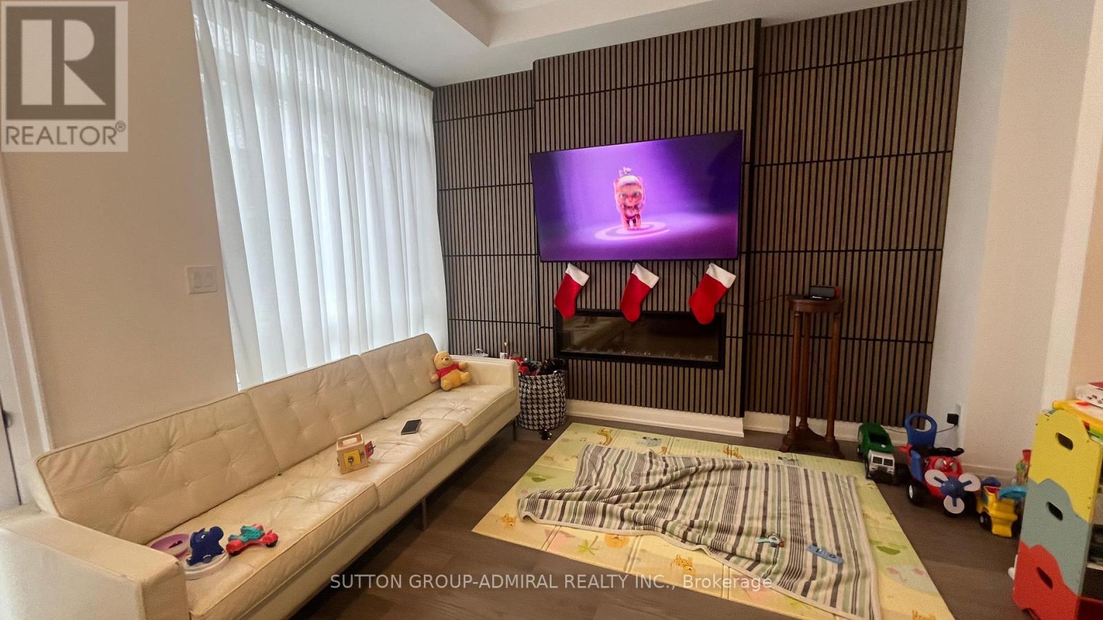 A living room with a white sofa, a fireplace, and a television displaying a cartoon character.