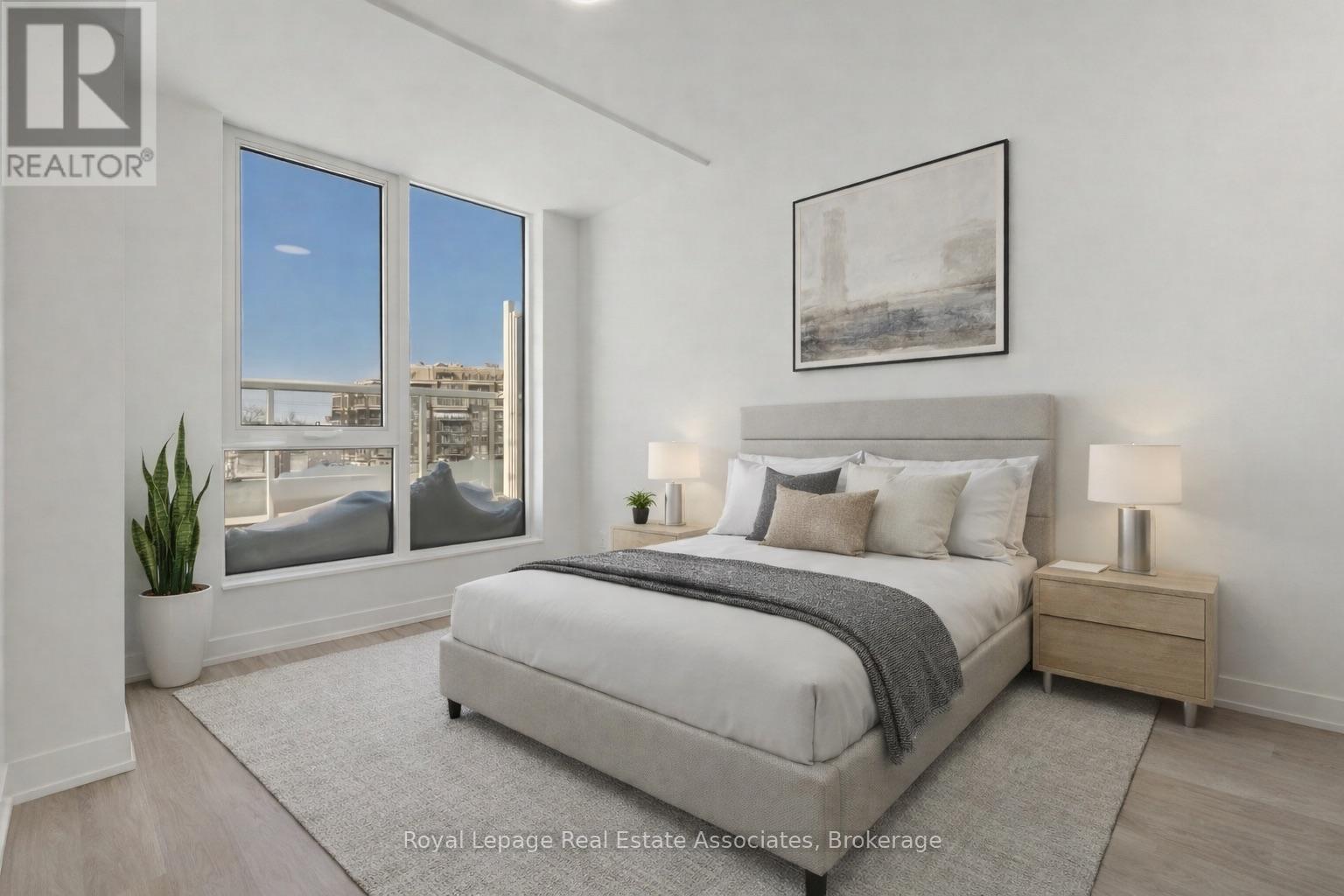 A bedroom with a large bed, a nightstand, and a window overlooking a cityscape.