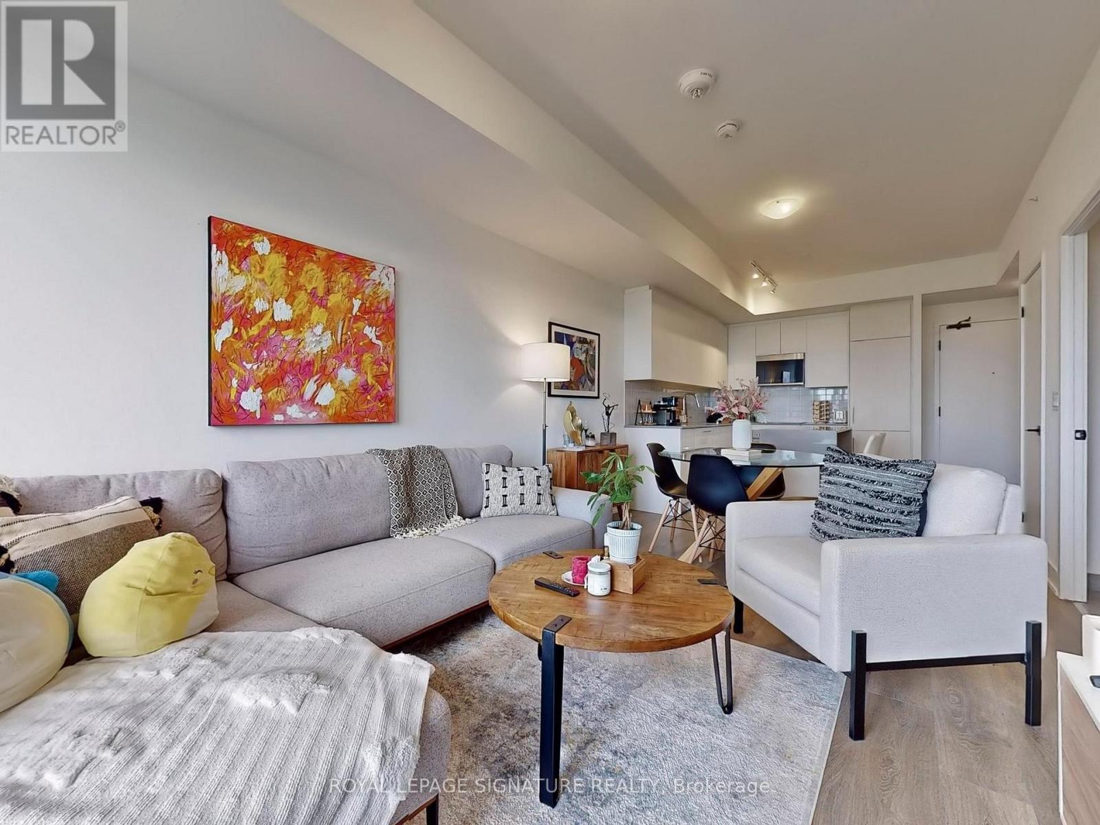 A living room with a grey couch, a yellow pillow, a coffee table and a painting on the wall.