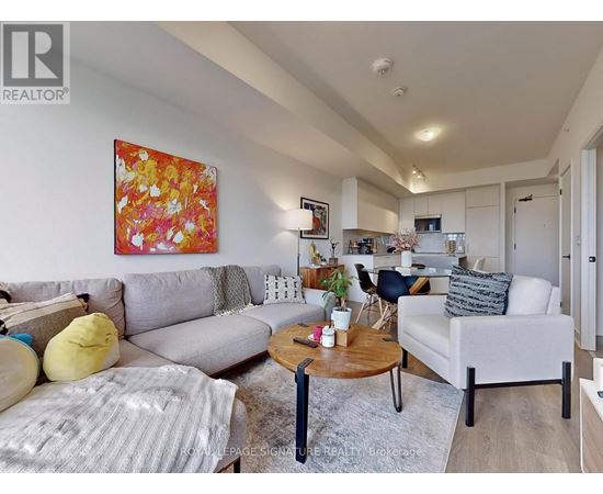 A living room with a grey couch, a yellow pillow, a coffee table and a painting on the wall.