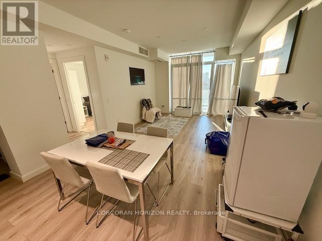 A well-lit, spacious room with a dining table and chairs, and a refrigerator.
