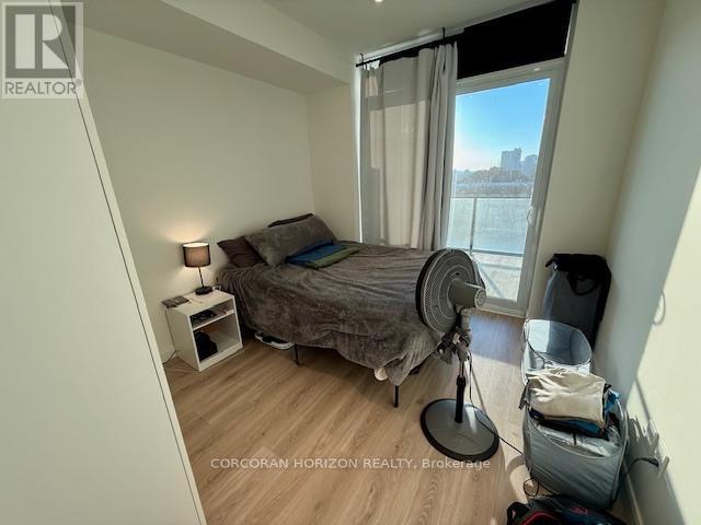 A bedroom with a bed, nightstand, and window with a view of the city.