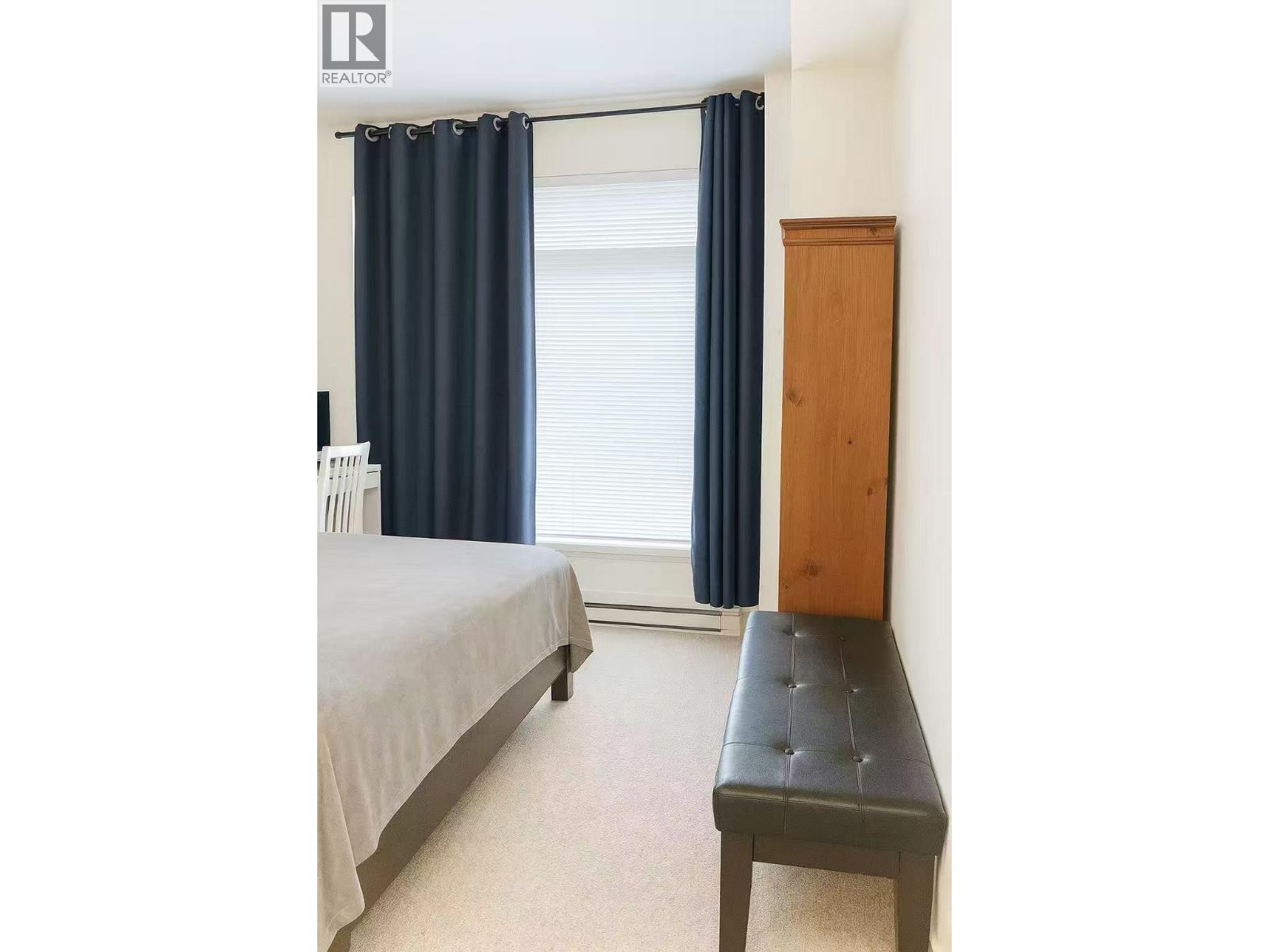 A bedroom with a bed, a bench, and a window with curtains.