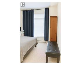 A bedroom with a bed, a bench, and a window with curtains.