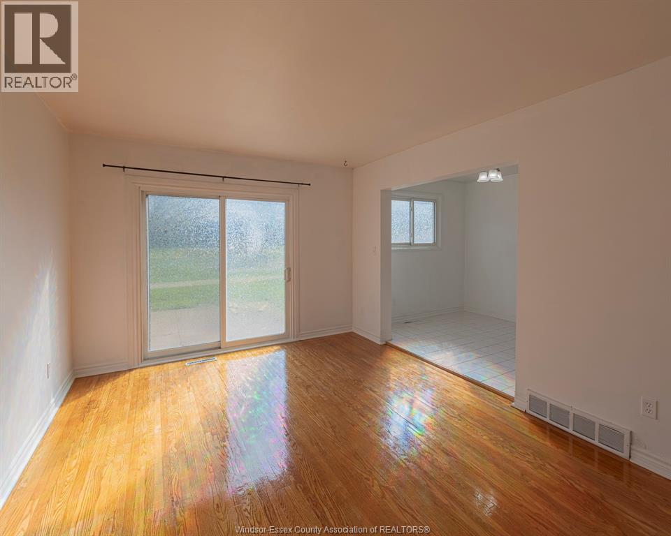 A room with wooden floors and white walls, with a sliding glass door leading to a green outdoor area.