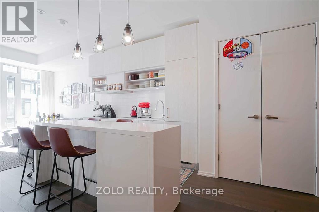 A kitchen with white cabinets and a countertop with a stove and two chairs.