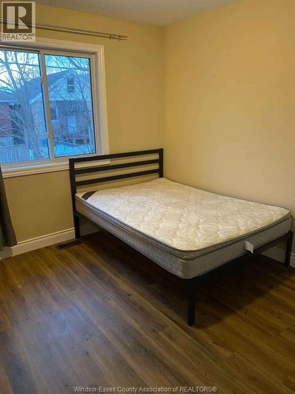 A bed with a white mattress and black frame in a room with wooden flooring.