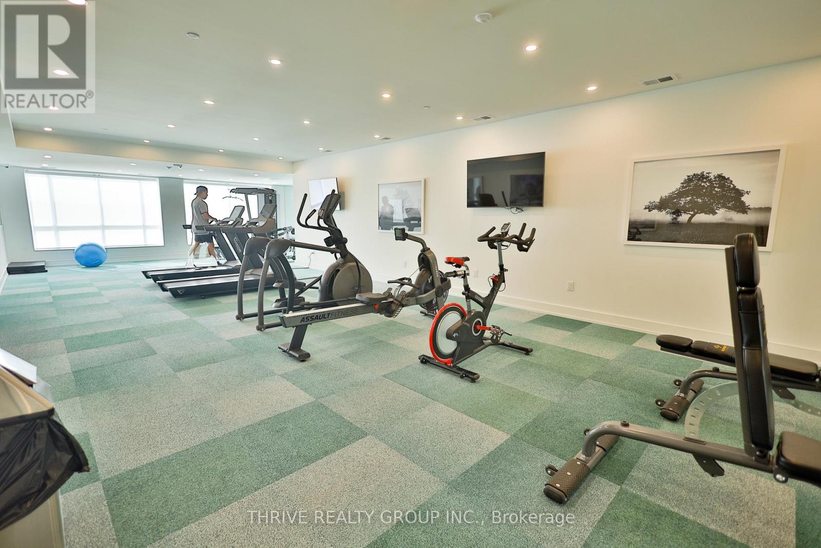 A gym with a green checkered floor and a person working out on a treadmill.