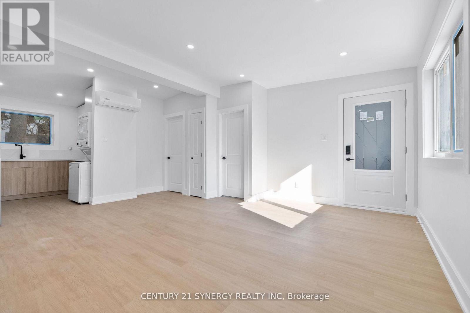 A spacious room with wooden flooring and white walls, with a door on the right side.