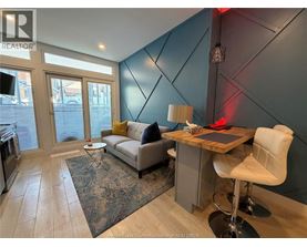 A living room with a grey couch, a white chair, and a wooden desk.