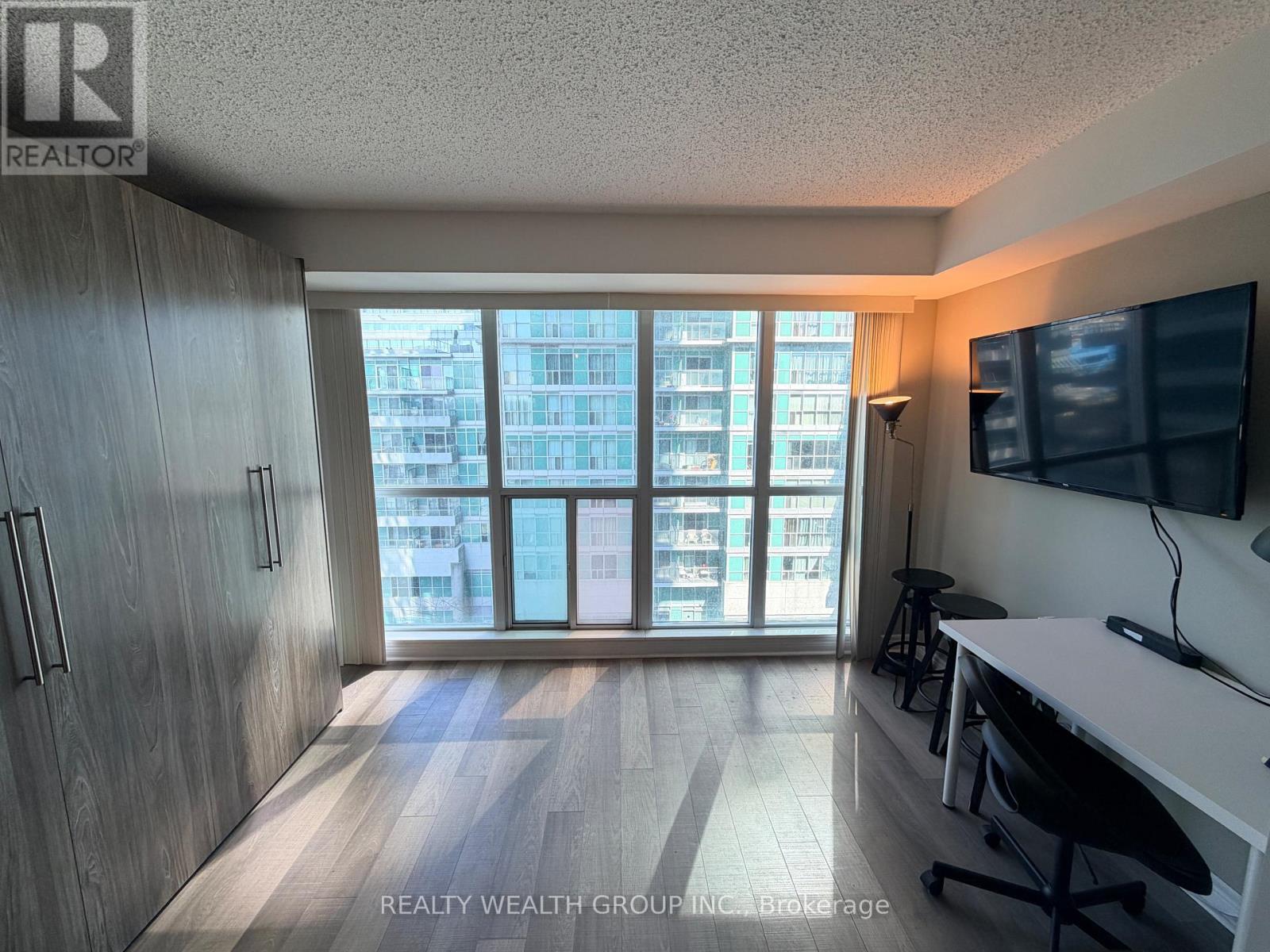 A room with a desk and a chair in front of a window with a view of a building.