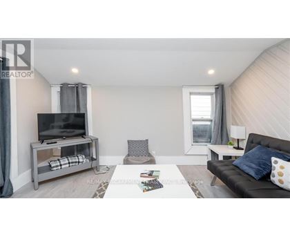 A living room with a grey couch, a television on a stand, and a window with curtains.