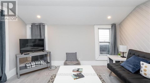 A living room with a grey couch, a television on a stand, and a window with curtains.