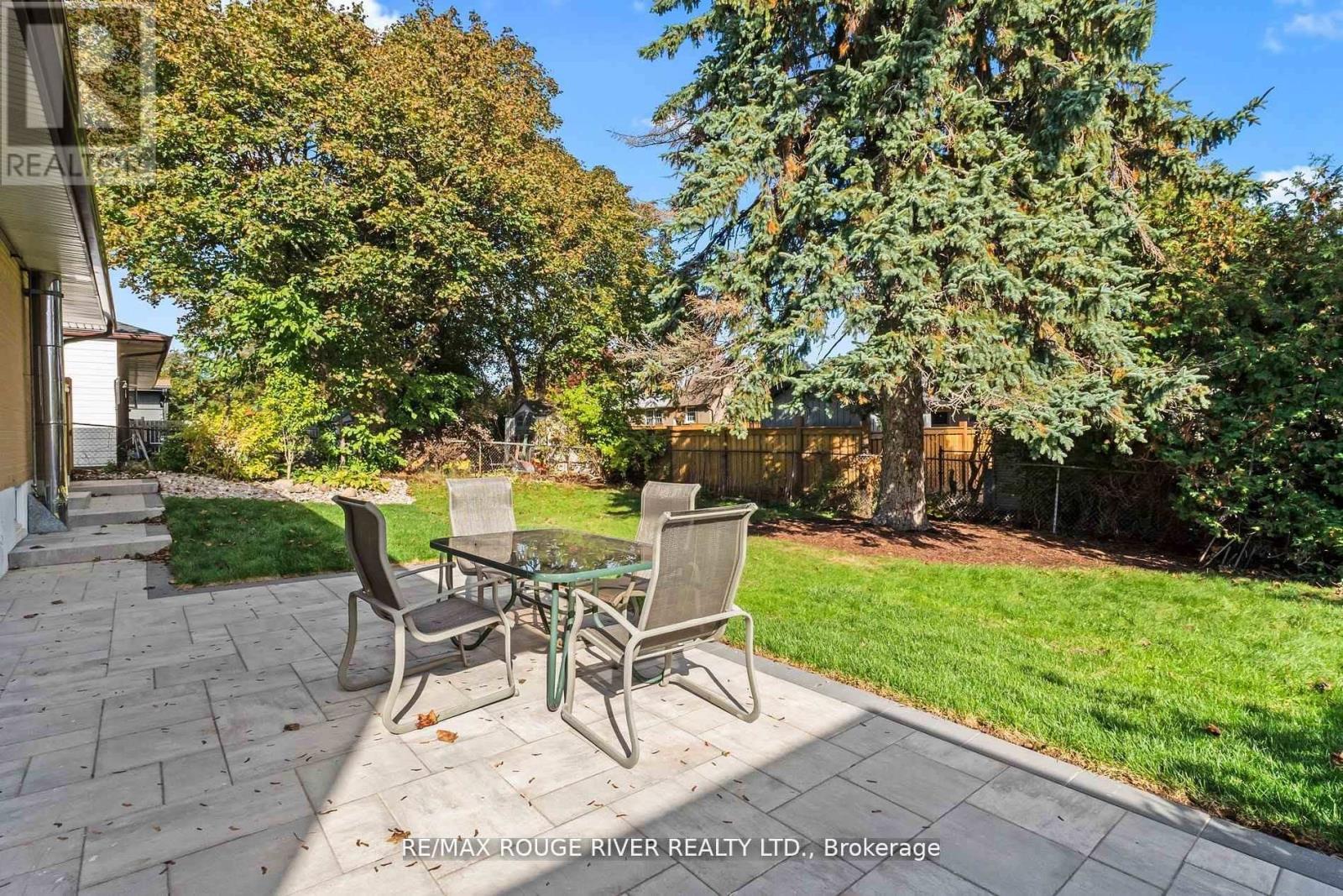 A patio with chairs and a table is surrounded by trees.
