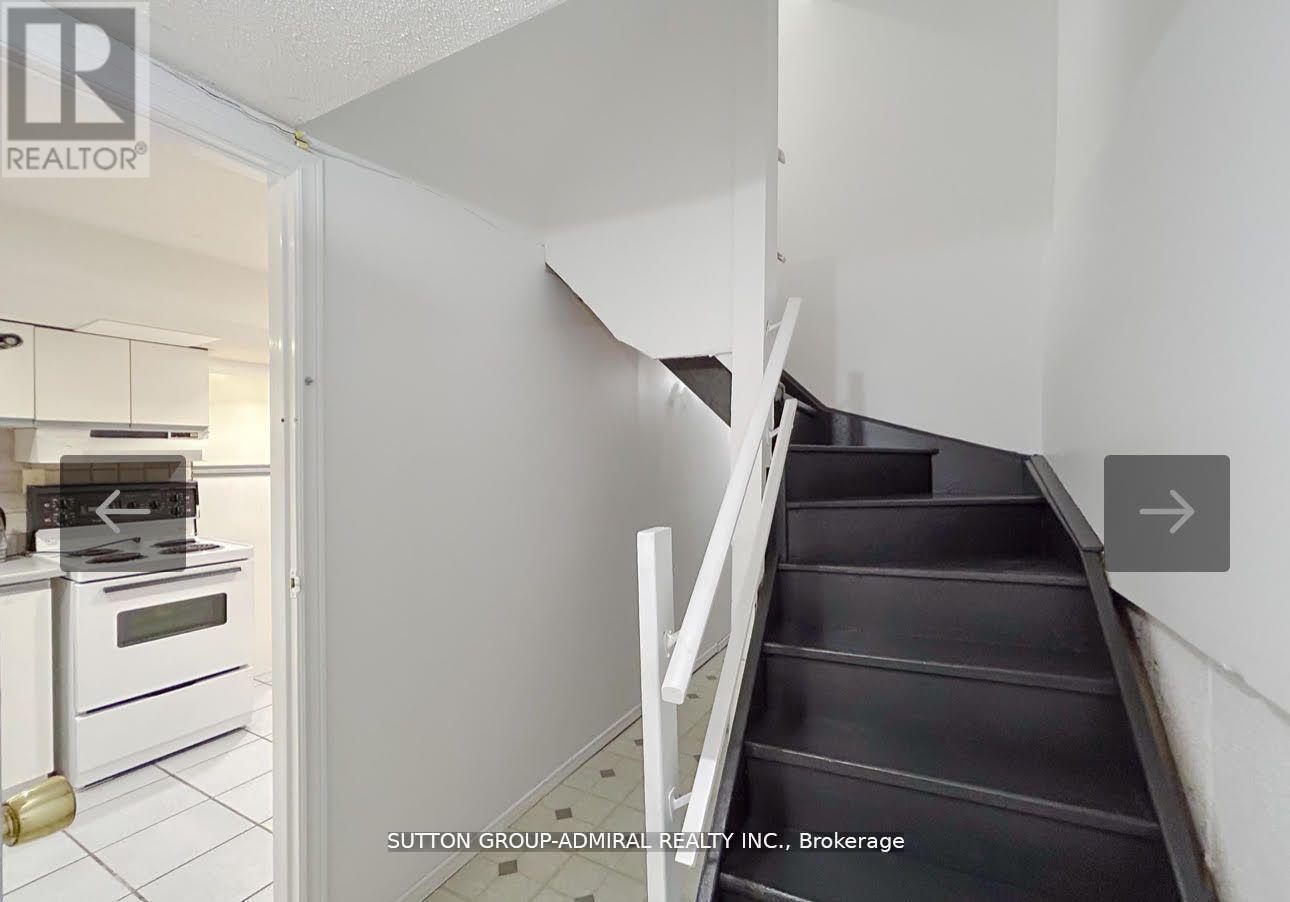 A staircase in a house with a white wall and a doorway leading to a kitchen.