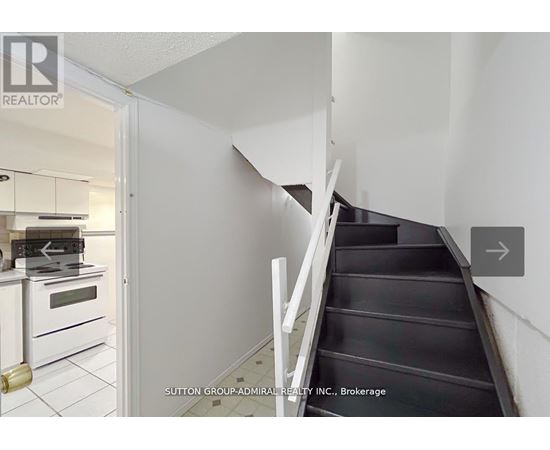 A staircase in a house with a white wall and a doorway leading to a kitchen.