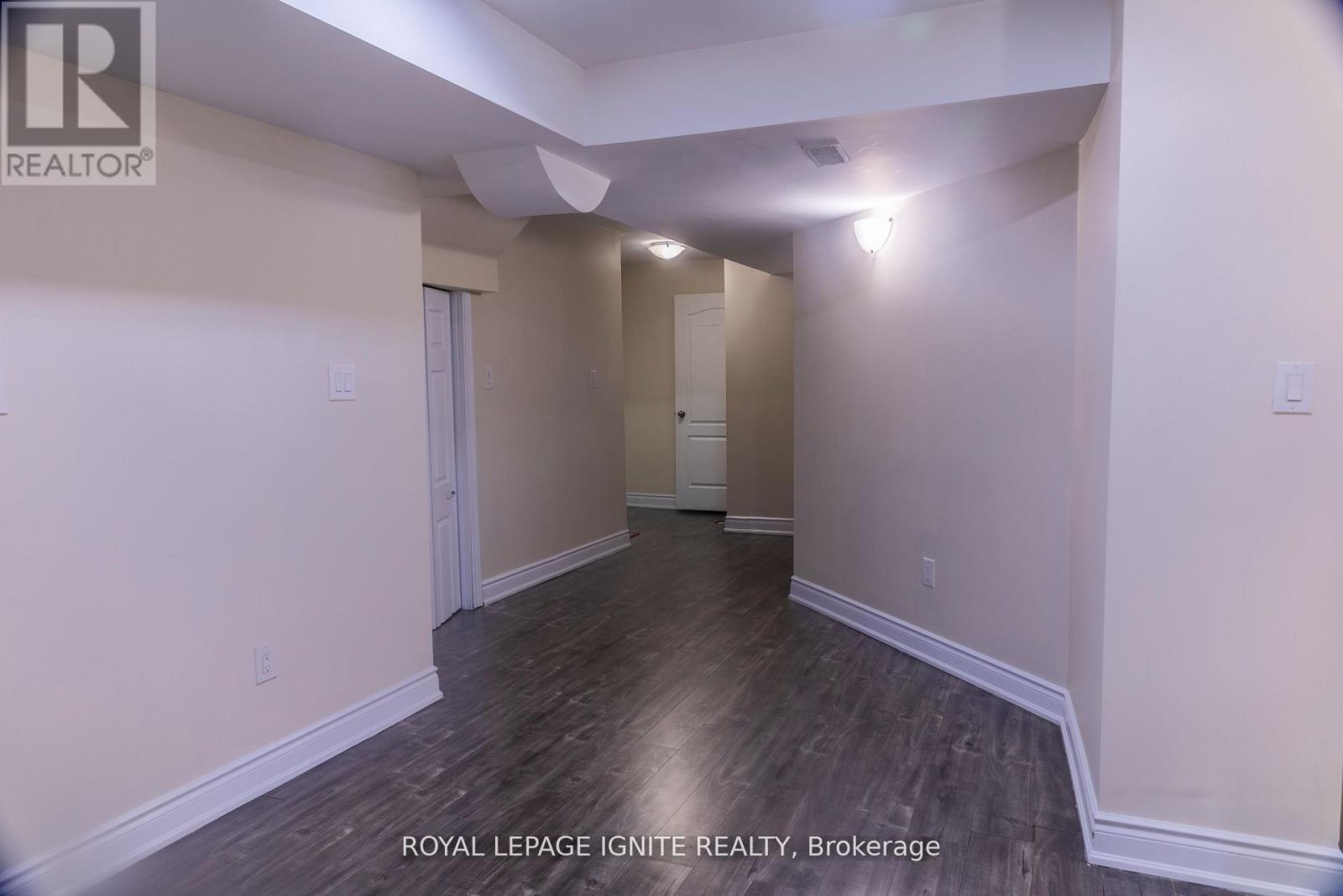 A room with wooden flooring and white walls, with a door on the left and a window on the right.