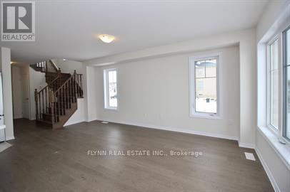 A spacious room with a staircase on the left and a window on the right.
