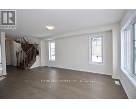 A spacious room with a staircase on the left and a window on the right.