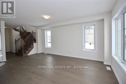 A spacious room with a staircase on the left and a window on the right.