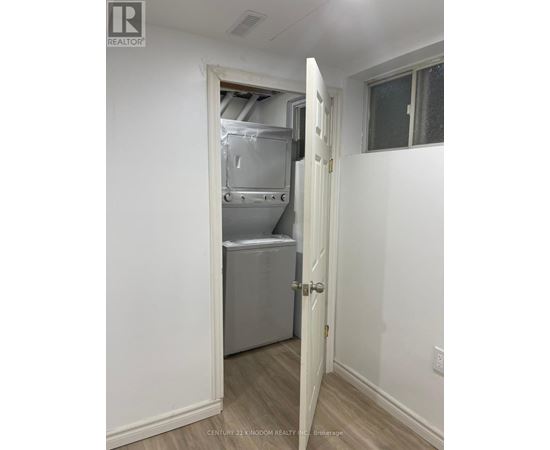 A white door is open to a small kitchen with a refrigerator and a cabinet.