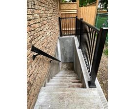 A set of stairs with a black railing and a brick wall on one side.