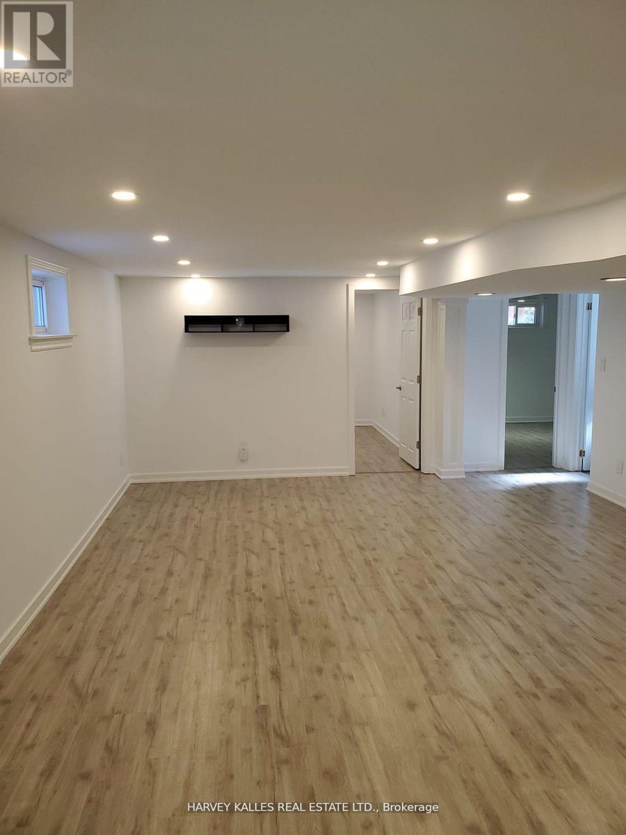 A room with wooden flooring and white walls, with a window on the left wall.