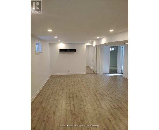 A room with wooden flooring and white walls, with a window on the left wall.