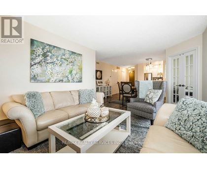 A living room with a beige couch, a glass coffee table, and a painting on the wall.