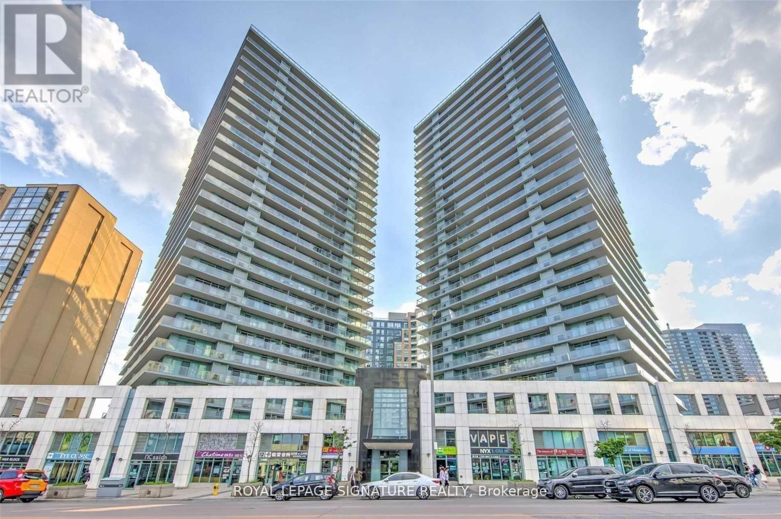 A tall building with a glass facade stands in the foreground of a street scene.