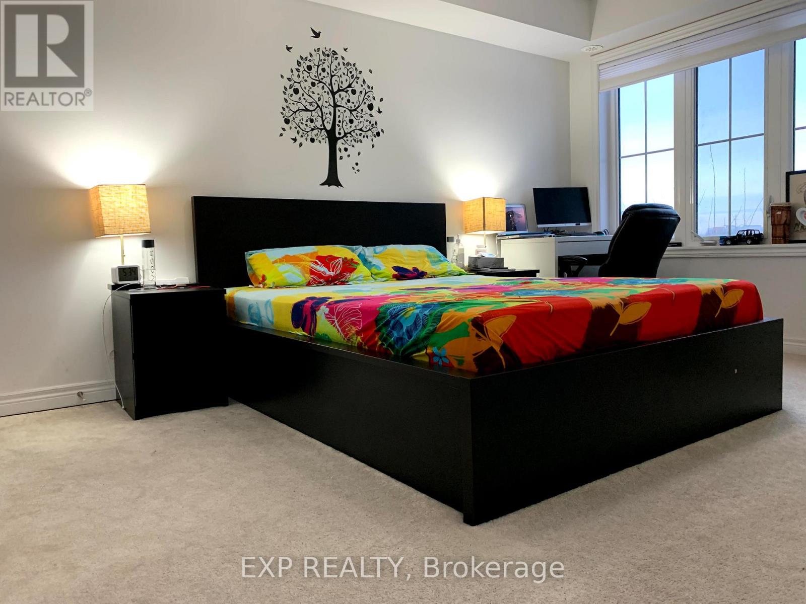 A bedroom with a black bed and a tree decal on the wall.