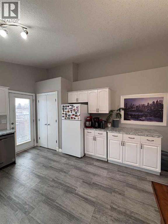 A kitchen with white cabinets and a fridge, a dining table with chairs, and a painting on the wall.