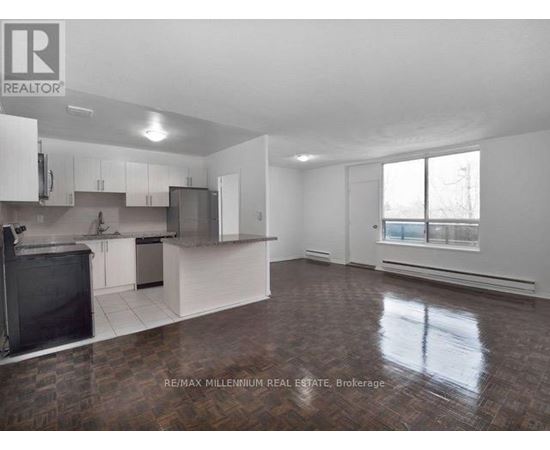 A large, empty room with a kitchen area and a window.