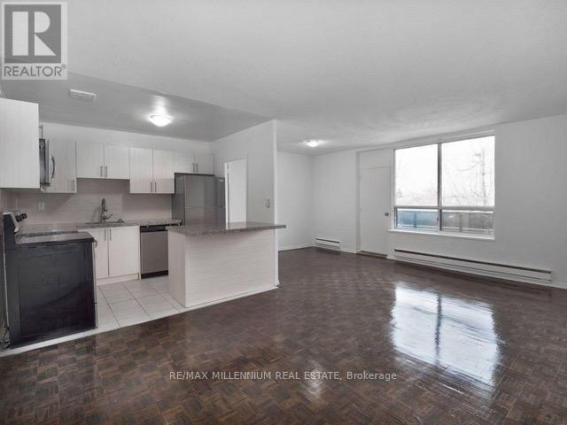 A large, empty room with a kitchen area and a window.