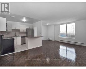 A large, empty room with a kitchen area and a window.