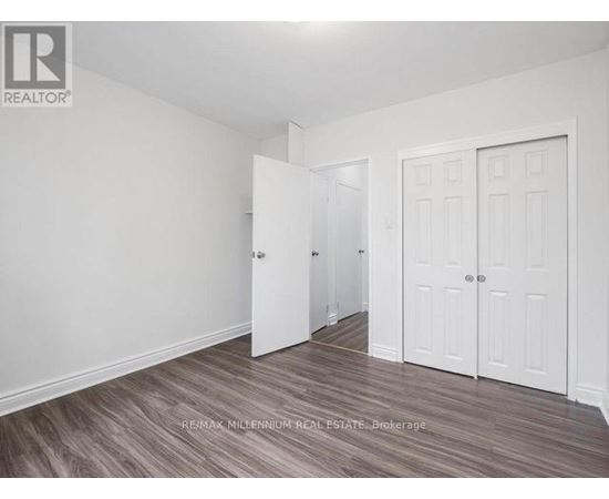 A room with white walls and a wooden floor with a brokerage logo.