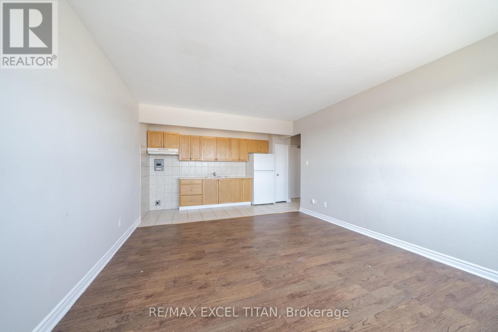 A spacious room with wooden flooring and white walls, featuring a built-in kitchenette.