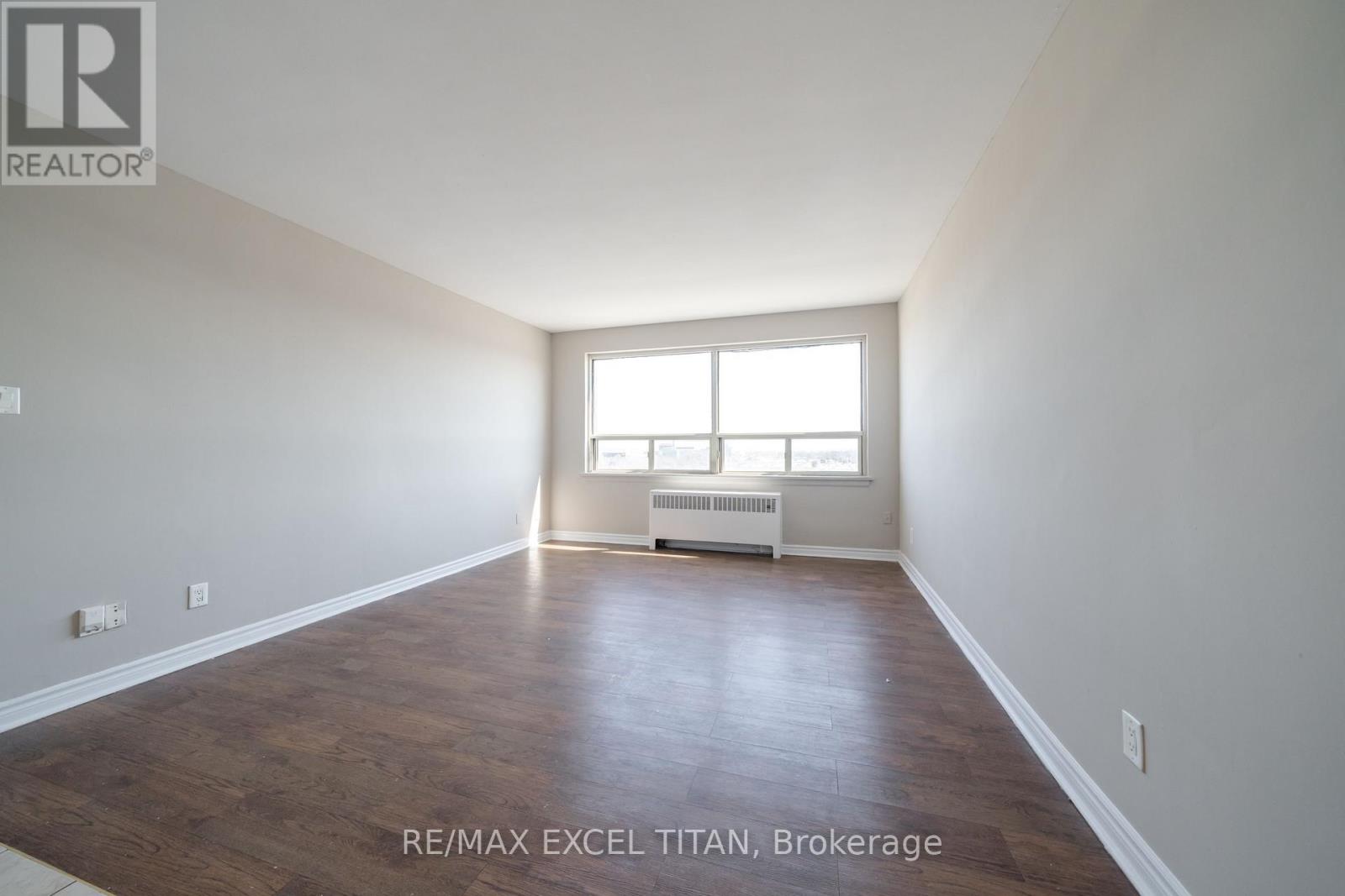 A spacious room with wooden flooring and a window with blinds.