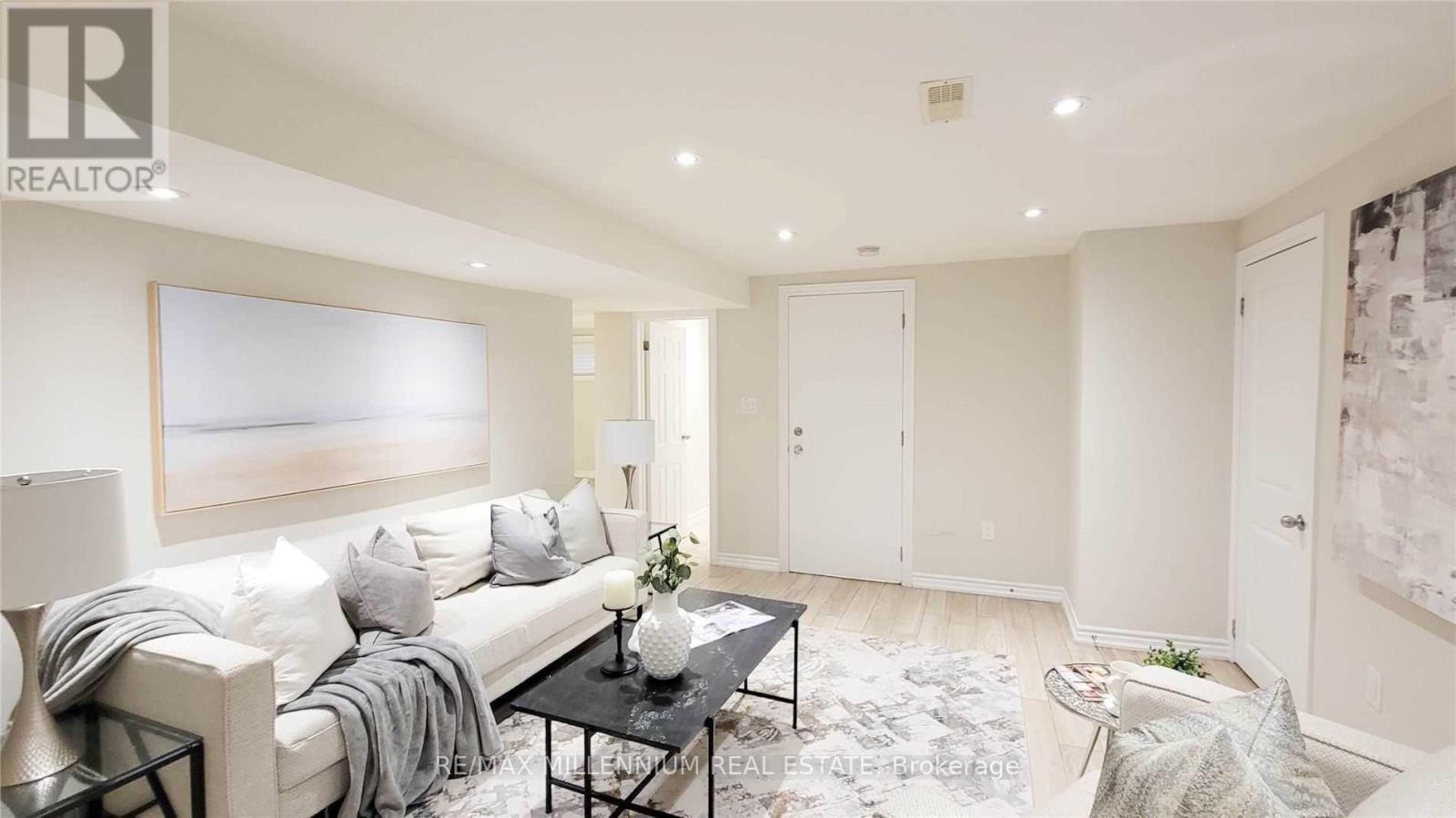 A well-lit, spacious living room with a white sofa, a coffee table, and a large painting on the wall.