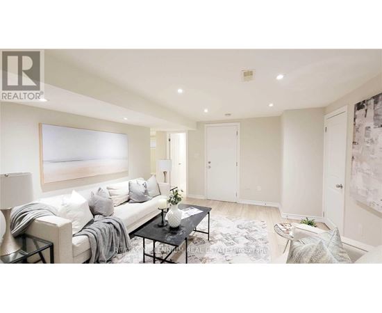 A well-lit, spacious living room with a white sofa, a coffee table, and a large painting on the wall.