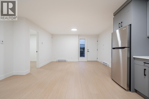A spacious kitchen with a refrigerator and wooden flooring.