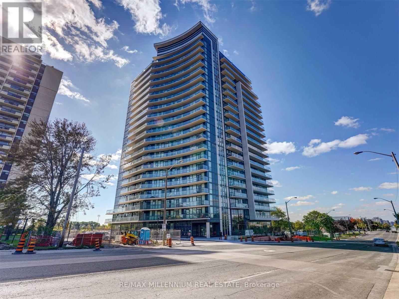 A modern multi-story building with a glass facade stands tall in the foreground of a sunny day.