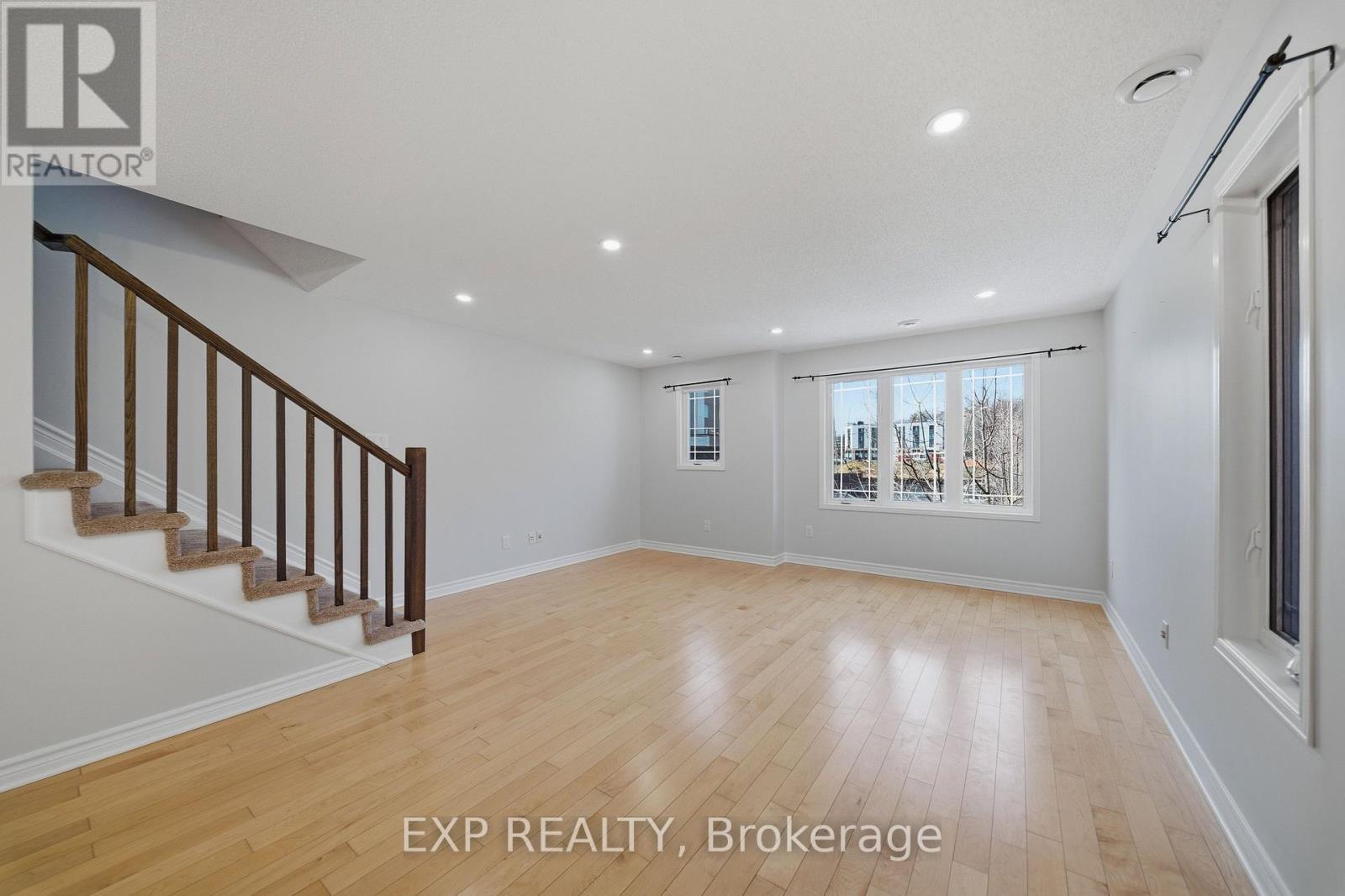 A spacious room with wooden flooring and a staircase with a railing.