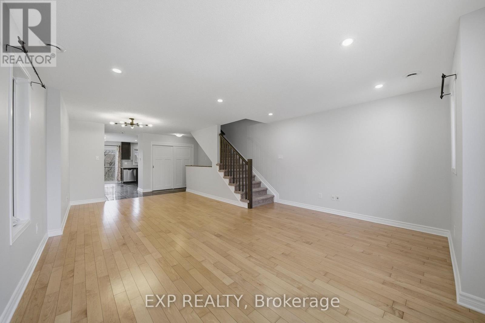A spacious room with wooden flooring and a staircase in the background.