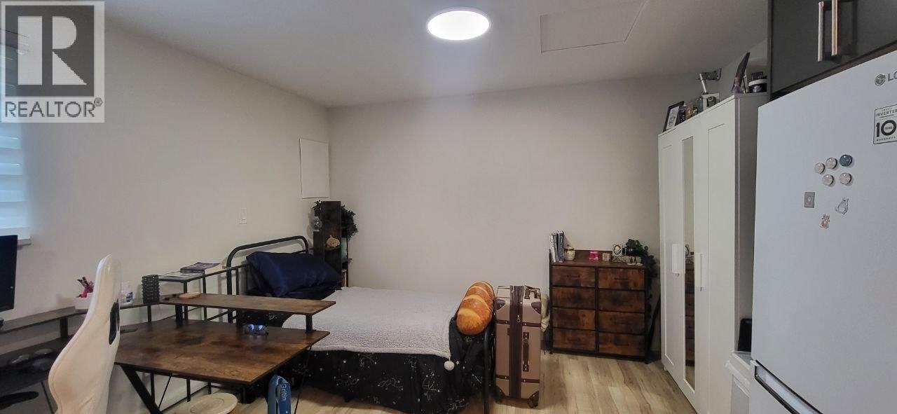 A bedroom with a bed, a chair, and a fridge.