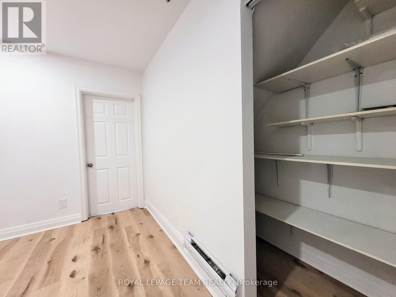 A white door is in a white room with a white wall and a white shelving unit.