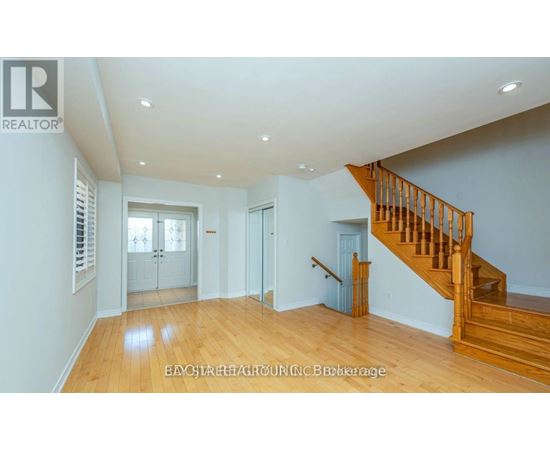 A spacious room with wooden floors and a staircase leading to another level.