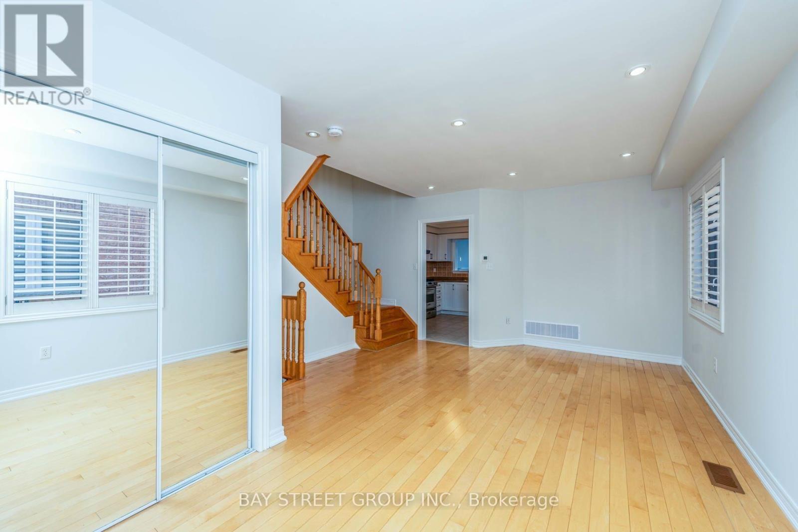 A spacious room with wooden floors and a staircase leading to another room.